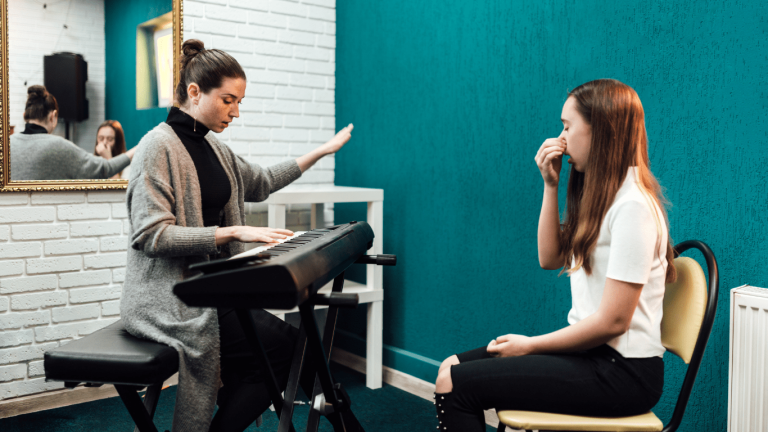 A music teacher playing a keyboard while a student practices breathing exercises