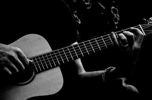 Black and white photo of a person's hands playing an acoustic guitar