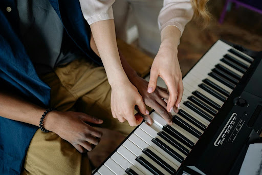 A teacher's hands guiding a student's hands on the keys of a digital piano