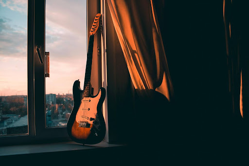 An electric guitar leaning against a window frame at sunset
