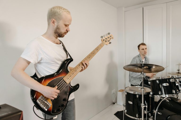 A man playing an electric bass guitar while a drummer sits behind a drum kit