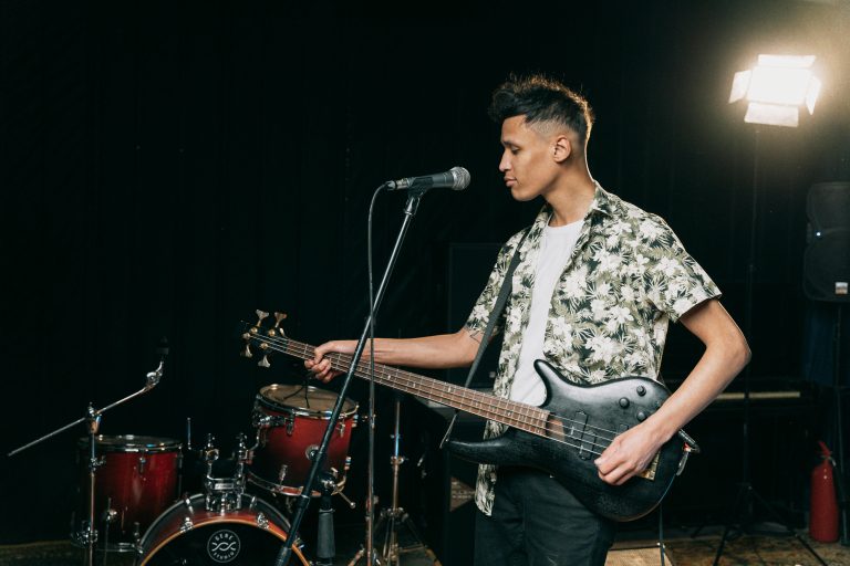 A man in a floral shirt playing a black electric bass guitar