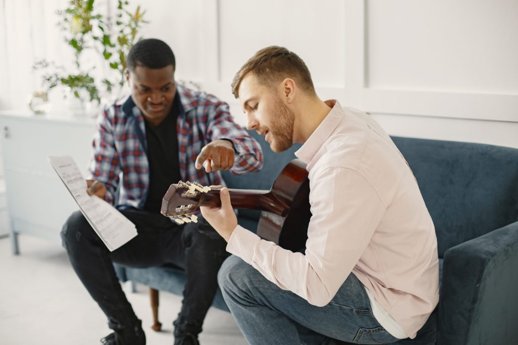 A man playing acoustic guitar and the other holding sheet music