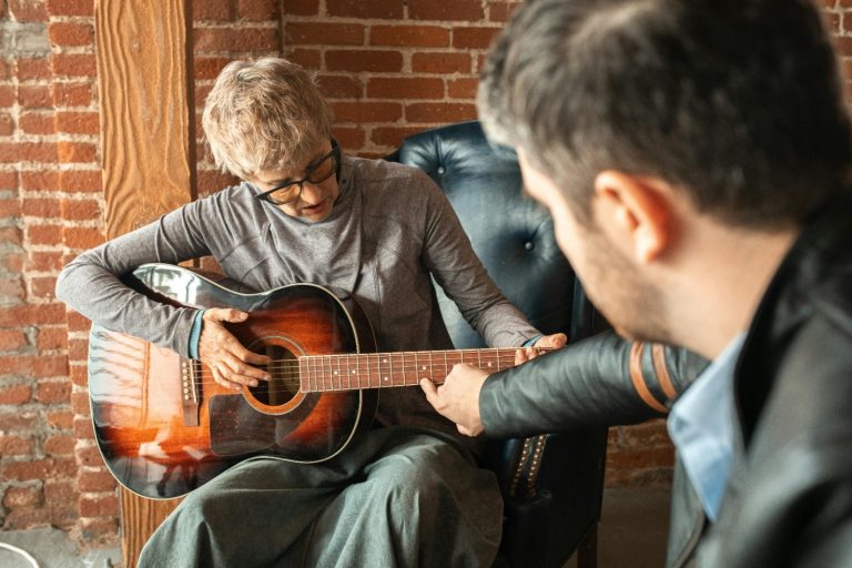 A woman playing acoustic guitar and a man pointing to the fretboard