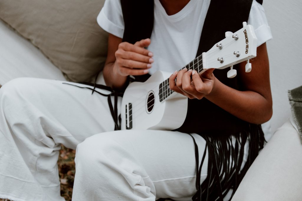 Person sitting down while playing a white ukulele