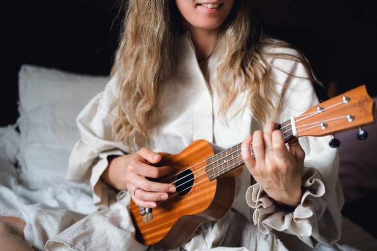Woman sitting in bed playing a wooden ukulele