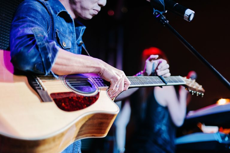 A musician in a denim shirt adjusting a capo on an acoustic guitar