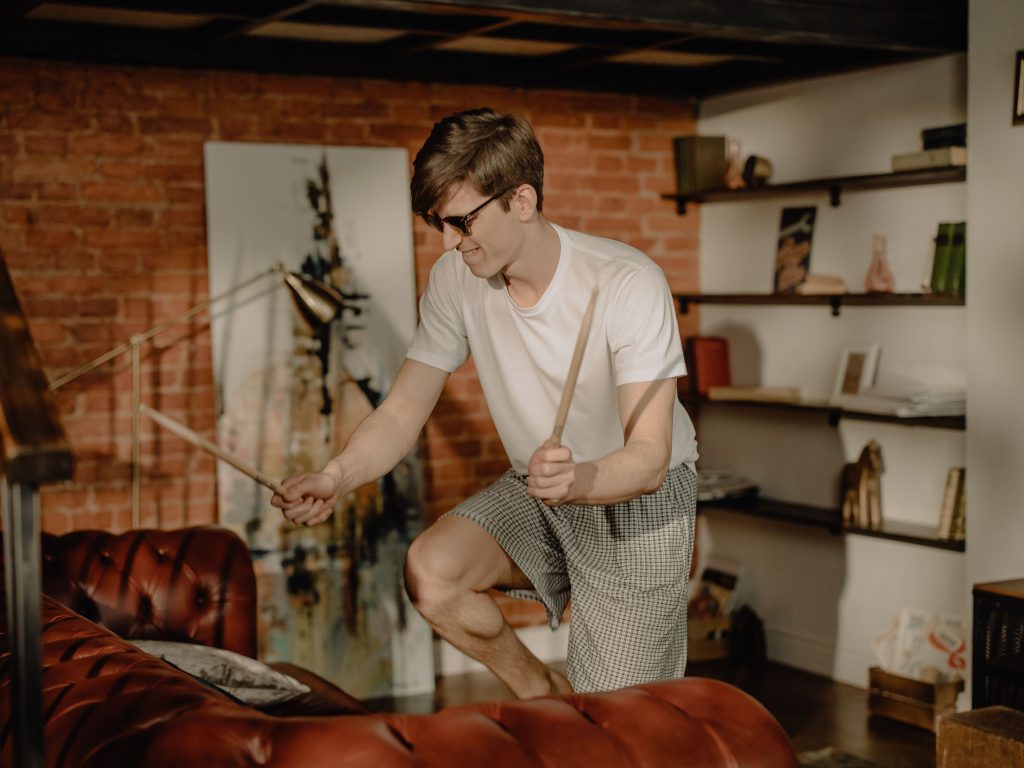 A man holding drumsticks and playing air drums near a sofa